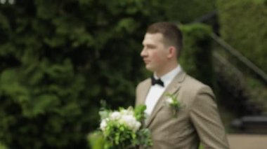 Damat, yeşil yaz parkında elinde düğün buketi olan genç bir adam. Sevgili gelinini bekliyor.