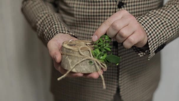 Groom in brown jacket holding wedding rings on wooden stand on the palm of hand. Man touches rings — Stock Video