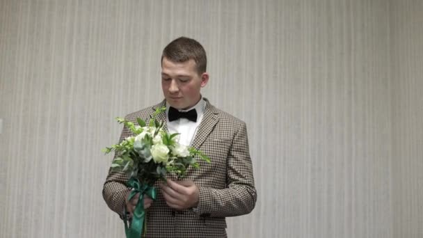 Novio con ramo de bodas en sus manos en casa. Camisa blanca, chaqueta — Vídeo de stock