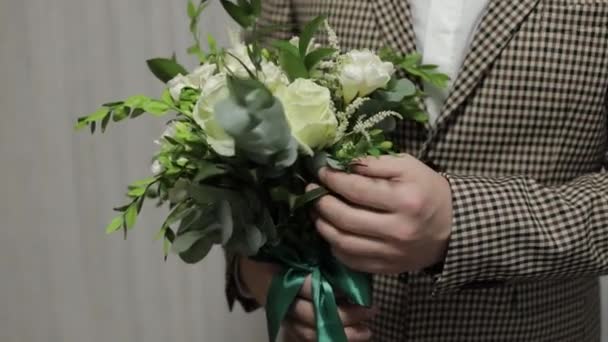 Novio con ramo de bodas en sus manos en casa. Camisa blanca, chaqueta. Primer plano de tiro. Movimiento lento — Vídeos de Stock