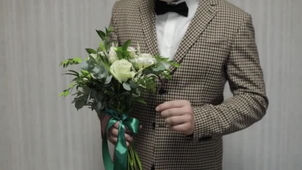 Γαμπρός με γαμήλια ανθοδέσμη στα χέρια του στο σπίτι. Λευκό πουκάμισο, σακάκι. Κοντινό πλάνο. Αργή κίνηση — Αρχείο Βίντεο