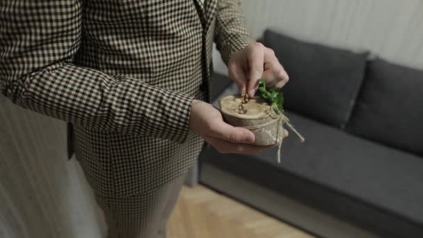 손에 나무 받침대에 결혼반지를 들고 있는 갈색 자켓을 입은 그 룸. 사람은 반지를 만진다 — 비디오