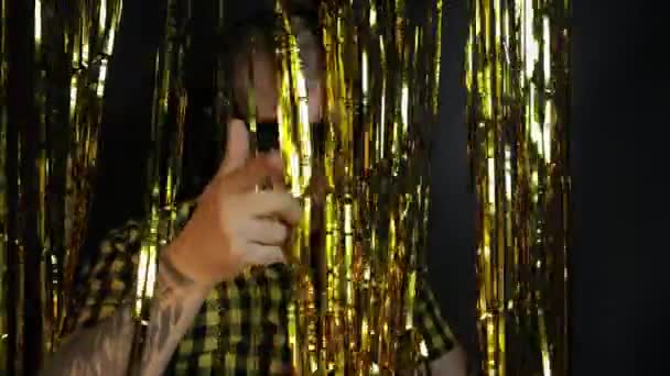 Porträt eines kaukasischen Mannes, der auf schwarzem Hintergrund tanzt. Goldglänzende Folienstreifen. Party, Musik, Disco — Stockvideo