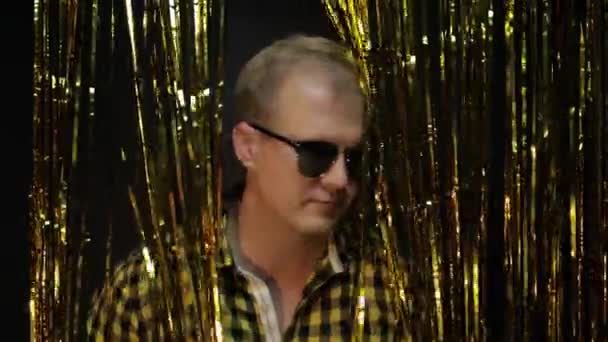 Portret białego mężczyzny pozującego na czarnym tle. Złote błyszczące paski foliowe. Impreza, muzyka, dyskoteka — Wideo stockowe