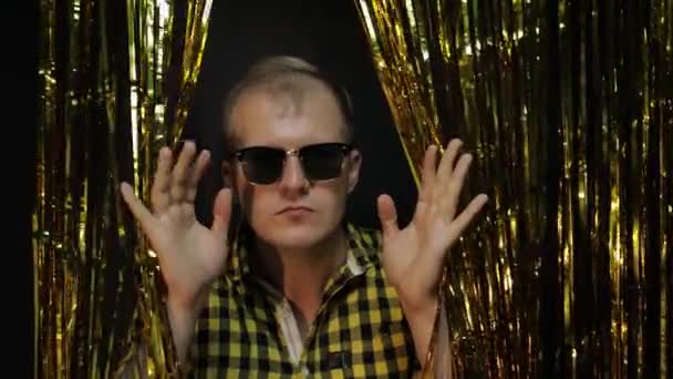 Portrét bělocha pózujícího na černém pozadí. Zlaté lesklé pruhy fólie. Party, hudba, diskotéka — Stock video