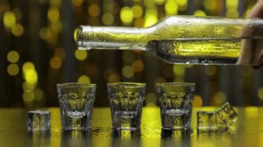 Barmen şişeden shot bardağına donmuş votka döktü. Pırıl pırıl altın parti geçmişine karşı buz küpleri