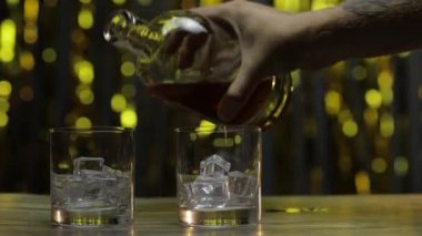 Viski, konyak ya da brendiyi şişeden buzlu bardaklara dök. Parlak arkaplan