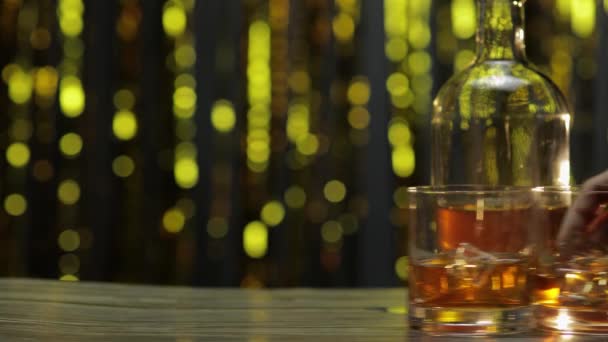 Бармен толкает, кладет два стакана с золотым виски, коньяком или бренди с кубиками льда на деревянный стол — стоковое видео