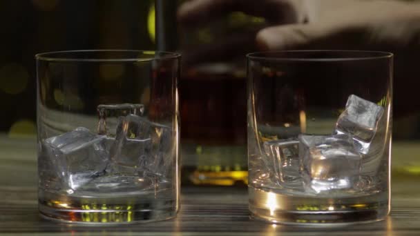 ウイスキー、コニャックまたはブランデーをボトルから氷のキューブでグラスに注ぐ。光沢のある背景 — ストック動画