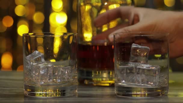 Giet whisky, cognac of cognac uit de fles in glazen met ijsblokjes. Glanzende achtergrond — Stockvideo