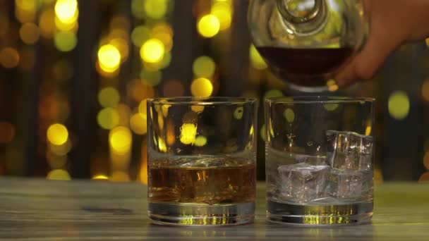 Versare il whisky dorato, il cognac o il brandy dalla bottiglia in un bicchiere con cubetti di ghiaccio. Sfondo lucido — Video Stock