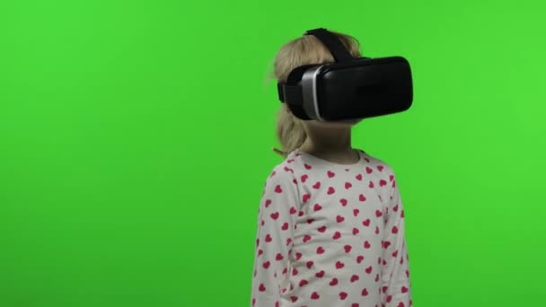 シミュレーションゲームアプリをプレイするVRヘルメットを使用して子供の女の子。仮想現実3Dビデオをご覧ください。クロマキー — ストック動画