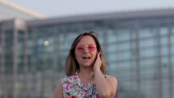 Mujer feliz turista en gafas de sol de moda bailando y escuchando música en el uso de auriculares smartphone — Vídeos de Stock
