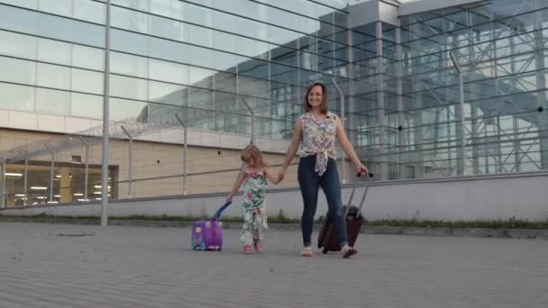 Anne ve kızı havaalanından yürüyerek geliyor. Bavul taşıyan kadın ve çocuk. Anne tatilden sonra — Stok video