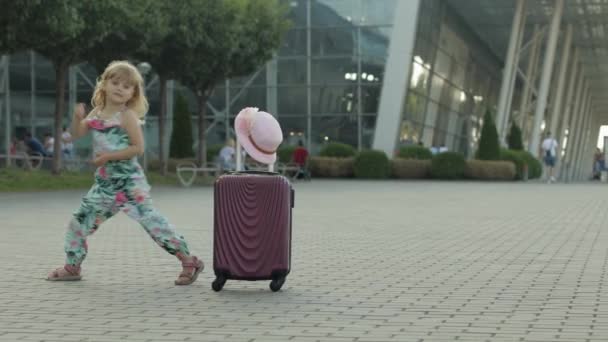 Child girl tourist with suitcase bag near airport. Kid dances, rejoices, celebrates with luggage — Stock Video