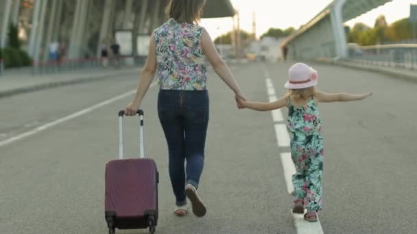 Madre e hija caminando al aire libre al aeropuerto. Una mujer que lleva una maleta. Vacaciones de niños y madres — Vídeo de stock