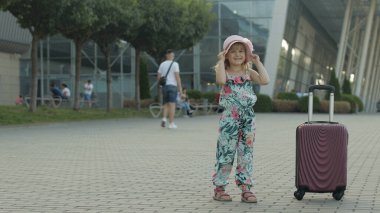 Çocuk turist havaalanının yanında bavul çantasıyla duruyor. Seyahate çıkar, tatile çıkar.