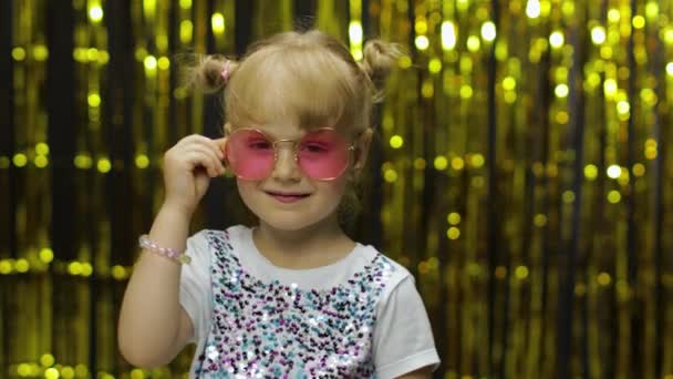 Criança sorrindo, apontando os dedos para a câmera. Menina posando no fundo com folha cortina dourada — Vídeo de Stock