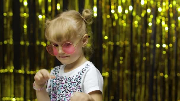 Enfant souriant, pointant du doigt la caméra. Fille posant sur le fond avec feuille rideau doré — Video