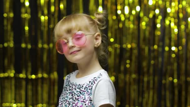 Kind glimlachend, kijkend naar de camera, vliegenzoen makend. meisje poseren op de achtergrond met folie gordijn — Stockvideo