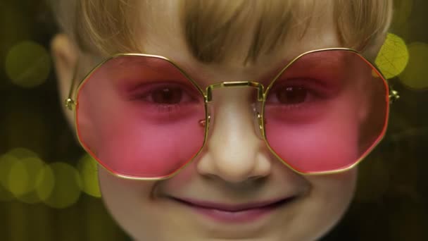 Gros plan visage de l'enfant. Souriant, regardant la caméra. Fille en rose lunettes de soleil posant — Video