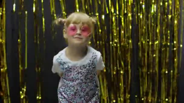 Child dancing, pointing fingers at camera. Girl posing on background with foil golden curtain — Stock Video