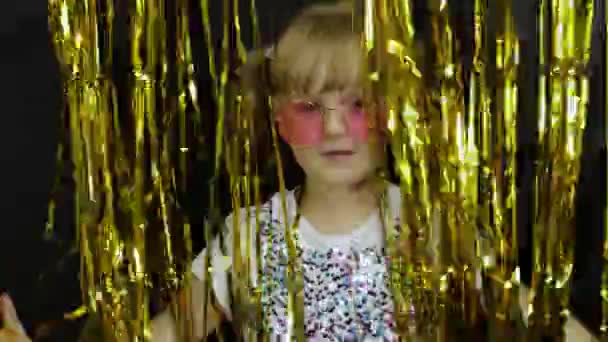 Happy child jumping, playing, fooling around in shiny foil fringe golden curtain. Little blonde kid — Stock Video