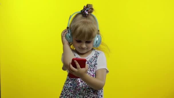 Child dances with smartphone, listening to music on headphones. Little kid girl dancing, having hun — Stock Video