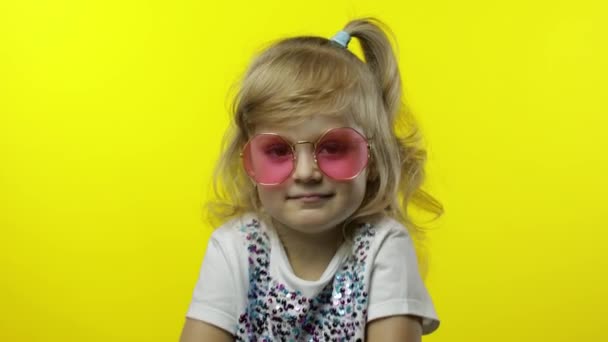 Lachend kind, kijkend naar de camera. Meisje toerist in roze zonnebril poseren op gele achtergrond — Stockvideo