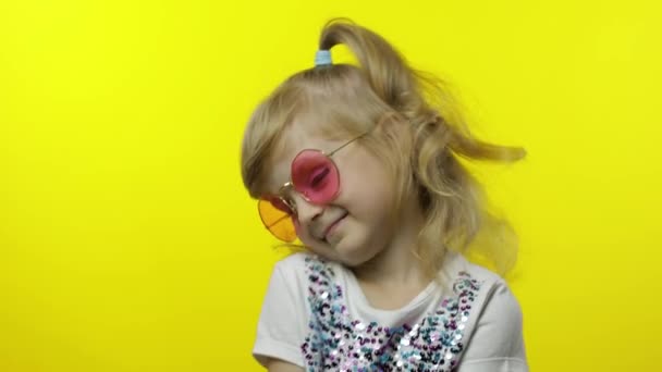 Lachend kind, kijkend naar de camera. Meisje toerist in roze zonnebril poseren op gele achtergrond — Stockvideo