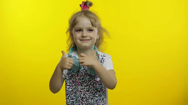 Dítě se sluchátky ukazují palce nahoru, usmívá se, demonstruje souhlas na žlutém pozadí — Stock fotografie