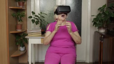 Sanal gözlüklü yaşlı büyükanne kadın evde 360 VR kaskla 3D video izliyor.
