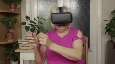 Sanal gözlüklü yaşlı büyükanne kadın evde 360 VR kaskla 3D video izliyor.