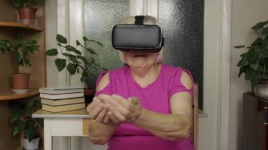 Sanal gözlüklü yaşlı büyükanne kadın evde 360 VR kaskla 3D video izliyor.