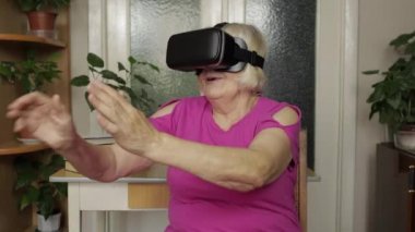 Sanal gözlüklü yaşlı büyükanne kadın evde 360 VR kaskla 3D video izliyor.