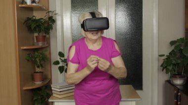 Sanal gözlüklü yaşlı büyükanne kadın evde 360 VR kaskla 3D video izliyor.