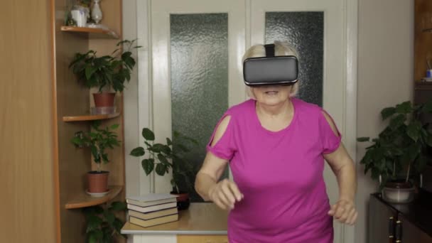 Старша бабуся в окулярах віртуальної гарнітури дивиться 3D відео в VR-шоломі і працює вдома — стокове відео