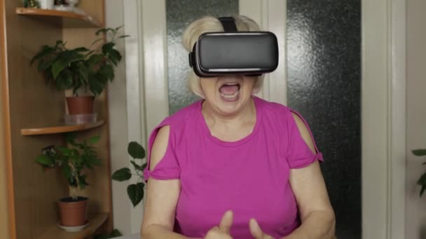 Senior grootmoeder vrouw in virtuele headset bril kijken 3d video in 360 vr helm thuis — Stockvideo