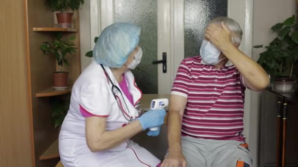 Nurse measures temperature with non-contact electronic thermometer of sick grandfather. Coronavirus — Stock Video