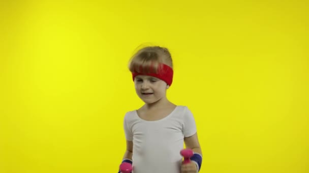 Белая девушка в спортивной одежде делает упражнения с гантелями. Тренировка для детей. Атлетическое дитя — стоковое видео