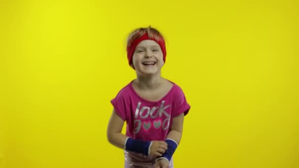 Pequeña chica caucásica feliz en ropa deportiva rosa sonríe, ríe. Entrenamiento para niños. Joven niño deportivo — Vídeos de Stock