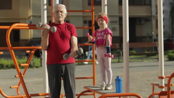 Nieta y abuelo haciendo ejercicios de fitness con pesas. Hombre mayor con niña niña — Vídeos de Stock