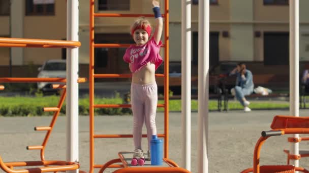 Niña linda joven en ropa deportiva haciendo ejercicios de gimnasta de fitness en el patio de recreo. Entrenamiento para niños — Vídeos de Stock