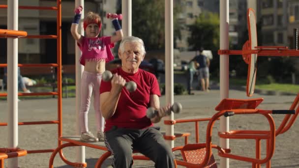 Granddaughter and grandfather doing fitness exercises with dumbbells. Senior man with child kid girl — Stock Video