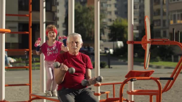 Neta e avô fazendo exercícios de fitness com halteres. Homem sênior com criança criança menina — Vídeo de Stock