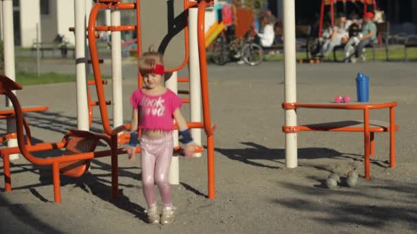 Młoda słodka dziewczynka w odzieży sportowej Dokonywanie ćwiczeń skok fitness na placu zabaw. Trening dla dzieci — Wideo stockowe