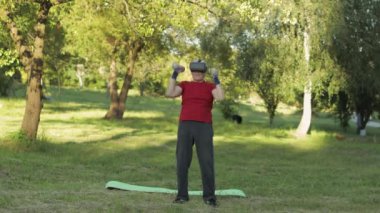 VR kulaklık takmış yaşlı bir dede dışarıda halterlerle spor yapıyor.