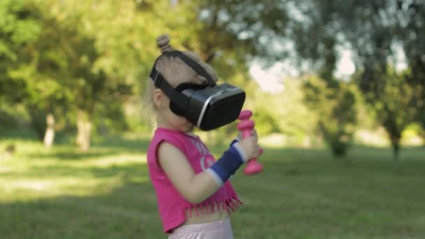 Menina atlética no capacete de fone de ouvido VR fazendo exercícios de fitness com halteres no parque — Vídeo de Stock