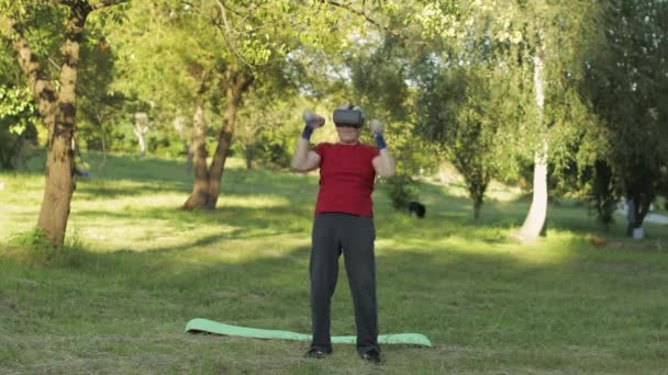 Sénior velho avô homem em VR capacete de fone de ouvido fazendo exercícios de fitness com halteres ao ar livre — Vídeo de Stock
