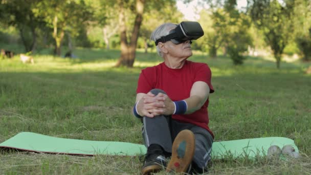 Starszy mężczyzna w kasku VR siedzi na macie sportowej. Trening sportowy online dla seniorów — Wideo stockowe